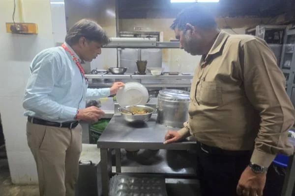होटल की रसोई में स्टील की मेज पर रखे भोजन के बर्तन को देखते दो पुरुष