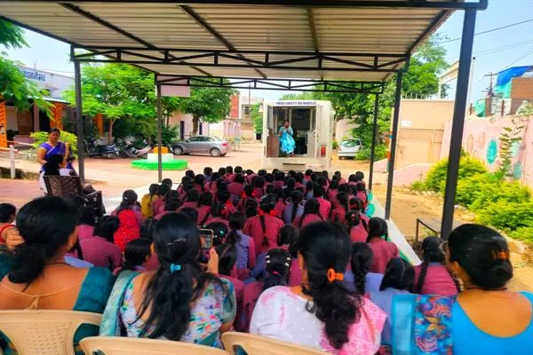 छतदार परिसर में कुर्सियों पर बैठी छात्राएं सामने खाद्य जागरूकता कार्यक्रम देखती हुईं