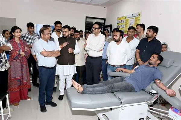 रक्तदान कुर्सी पर लेटे एक रक्तदाता के पास खड़े अधिकारी और अन्य लोग