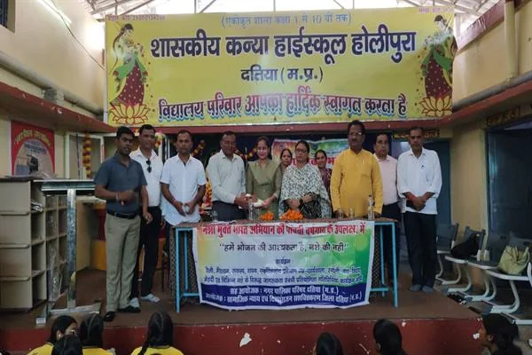 स्कूल के मंच पर नशामुक्ति संदेश वाले बैनर के पीछे खड़े अधिकारी, शिक्षक और अन्य प्रतिभागी