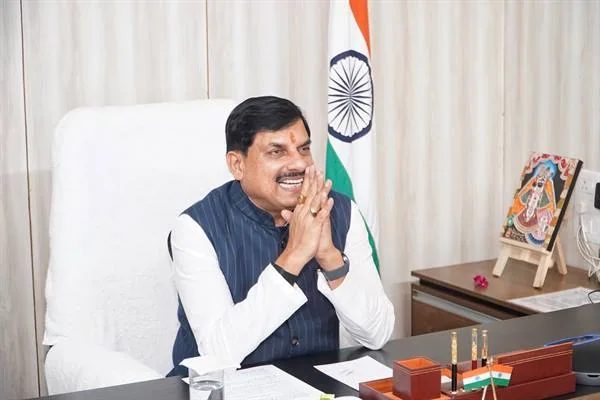 कार्यालय में मेज के पीछे बैठे मुख्यमंत्री डॉ. मोहन यादव हाथ जोड़कर मुस्कुराते हुए, पीछे भारतीय ध्वज