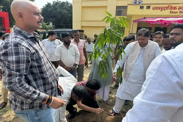 स्वास्थ्य केंद्र परिसर में एक पौधे के पास खड़े लोग और मिट्टी में पौधरोपण करते दो व्यक्ति