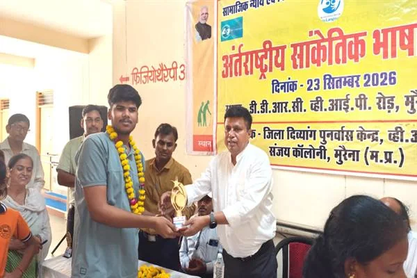 मुरैना के जिला दिव्यांग पुनर्वास केंद्र में एक युवक को ट्रॉफी सौंपते अधिकारी, पीछे सांकेतिक भाषा दिवस का बैनर लगा है